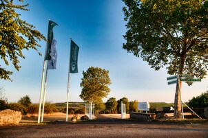 Una entrada rural con banderas, un cartel de Landhotel Kauzenberg y un camino que conduce a la propiedad.