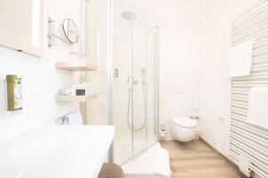 Un baño moderno con cabina de ducha de vidrio, inodoro blanco y suelo de madera.