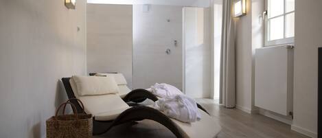 A spa room with a massage table, a wicker basket, and a shower area.
