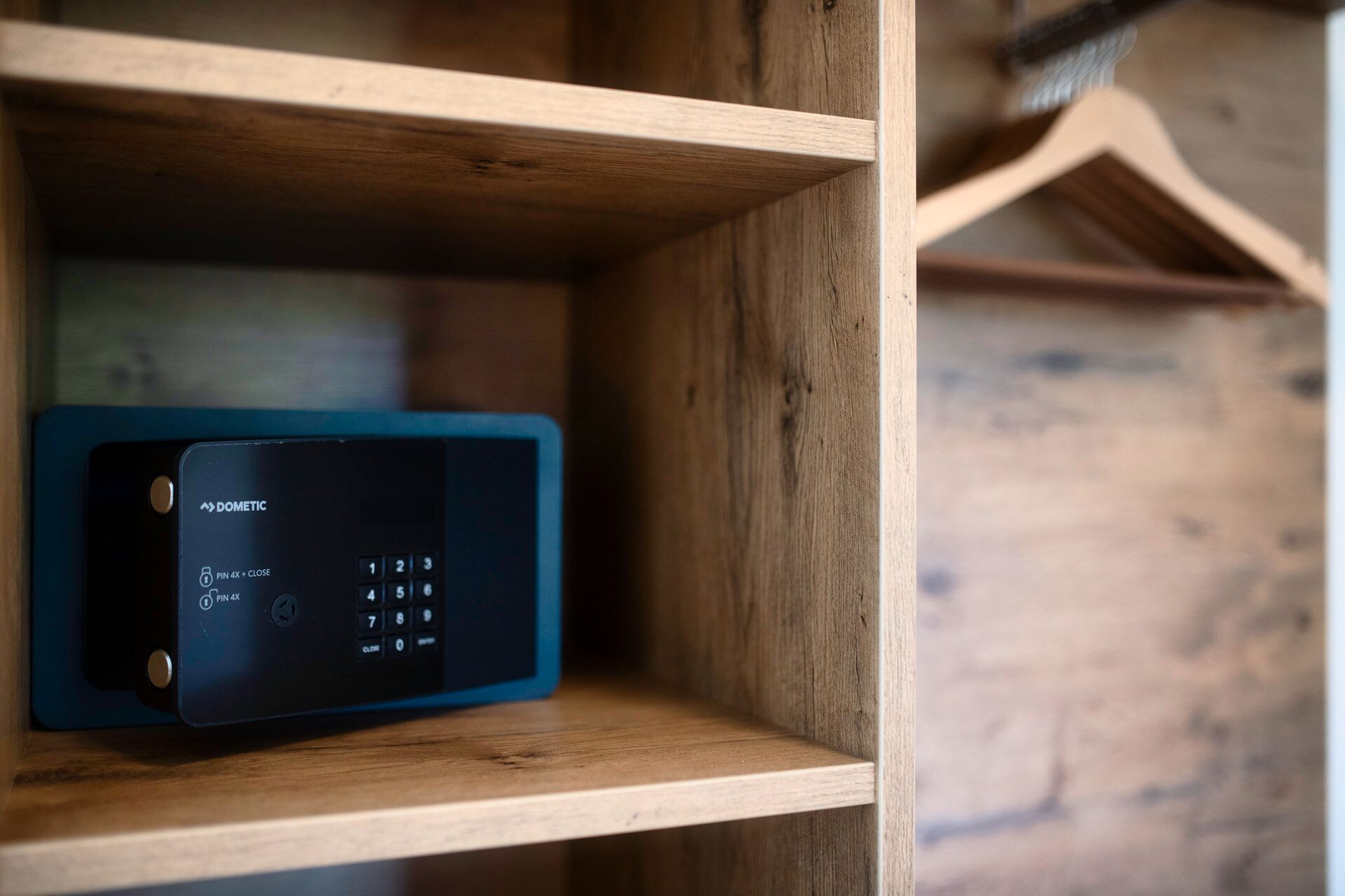 A black electronic device with a keypad and PIN options on a wooden shelf.