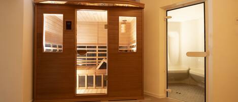 A sauna room with wooden walls and a glass door leading to a shower area.