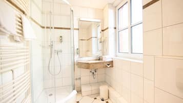 Un baño con ducha acristalada, lavamanos con encimera de granito y ventana que proporciona luz natural.