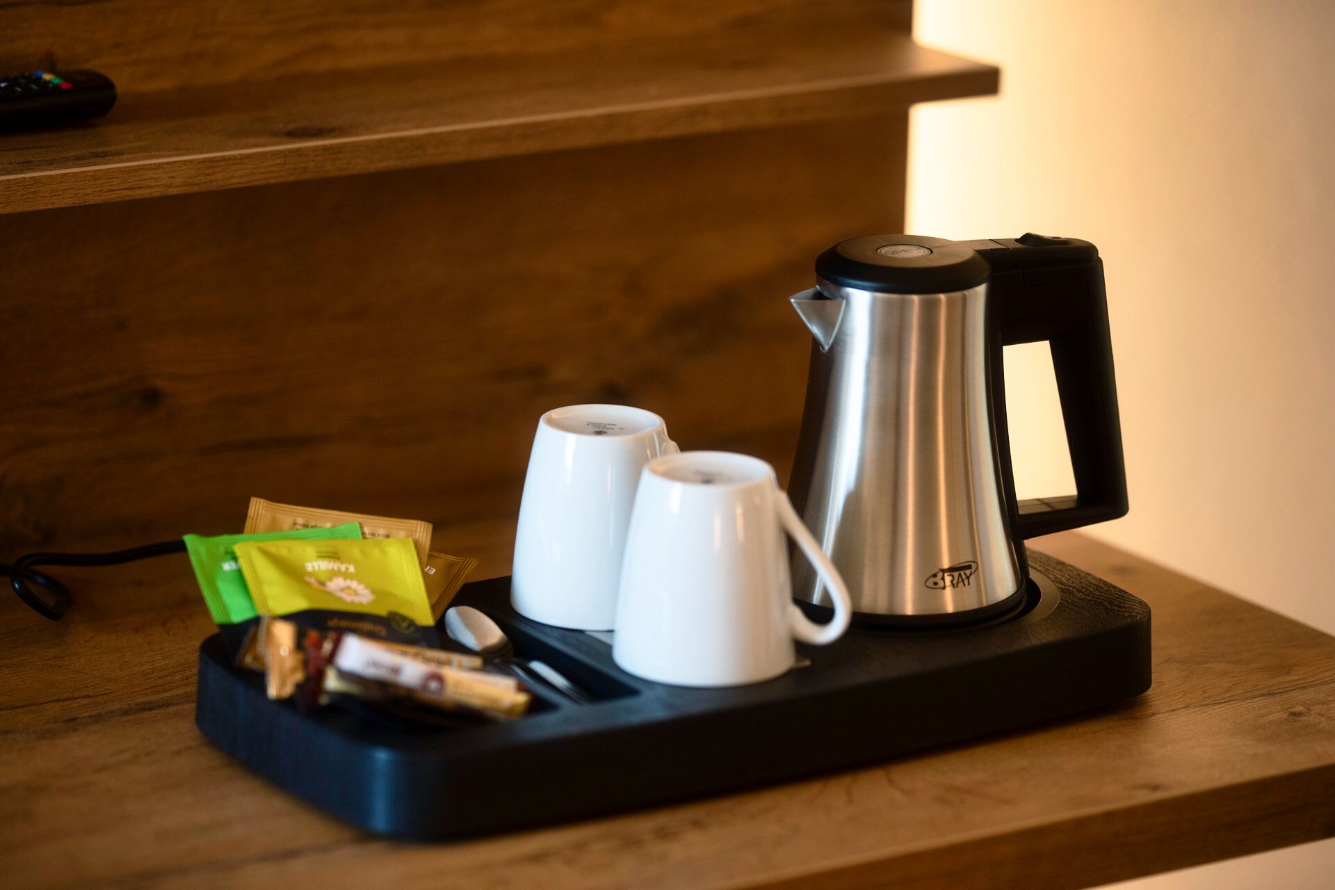 Eine Kaffeemaschine, zwei weiße Tassen und eine Serviertschale mit Snacks auf einem Holztisch.