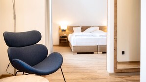 Ein modernes Hotelzimmer mit blauem Sessel, einem Bett mit weißer Bettwäsche und einem Nachttisch mit Lampe.