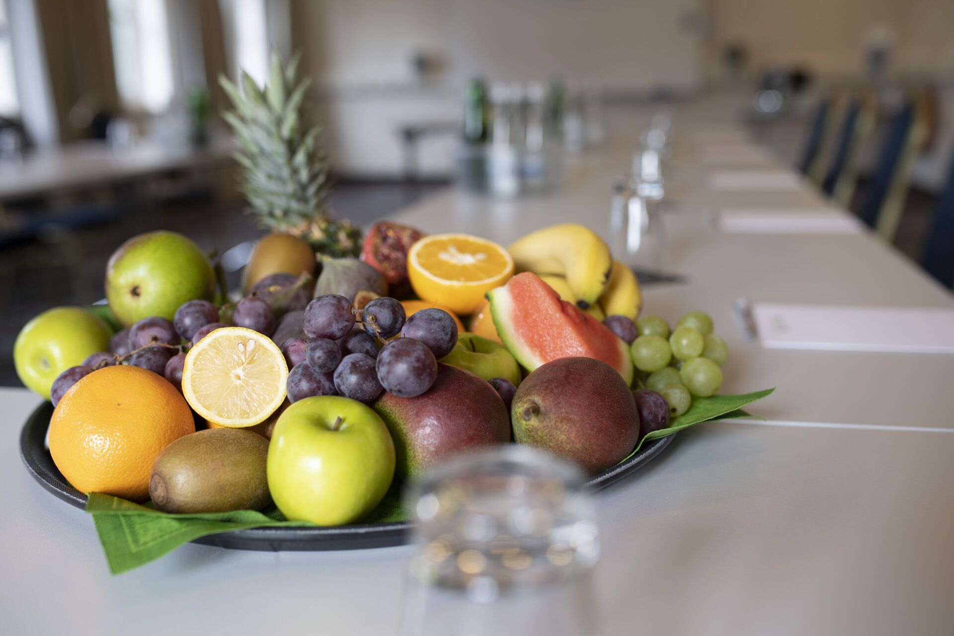 Une assiette de fruits est posée sur une table, et elle contient une variété de fruits, notamment des pommes, des oranges, des raisins et une tranche de pastèque.