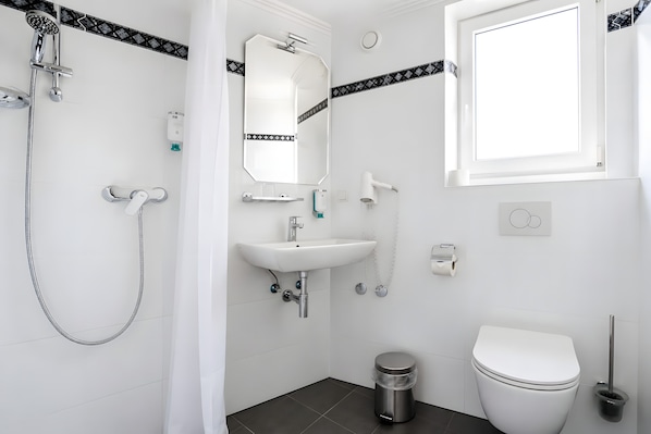 A modern bathroom with a shower, sink, toilet, and a window.