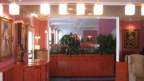 Zona de recepción de hotel con mostrador de mármol, cuadros enmarcados y una planta grande en maceta.