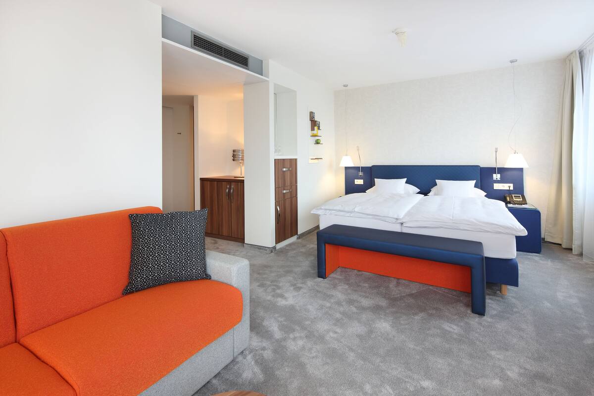 A modern hotel room with a bed, a sofa, and a desk.