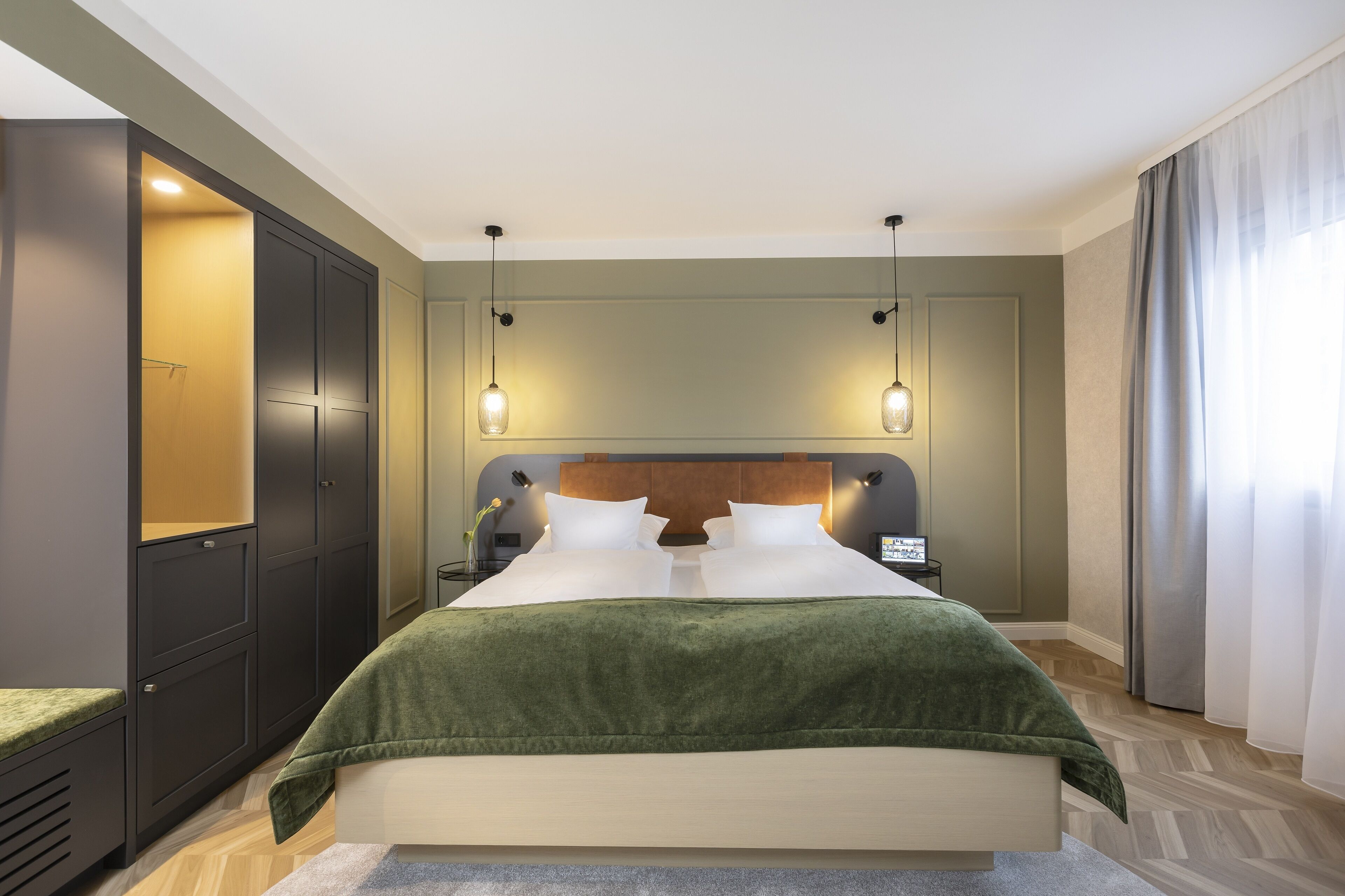 Una habitación de hotel moderna con una cama grande, un armario y una mesita de noche con lámpara.
