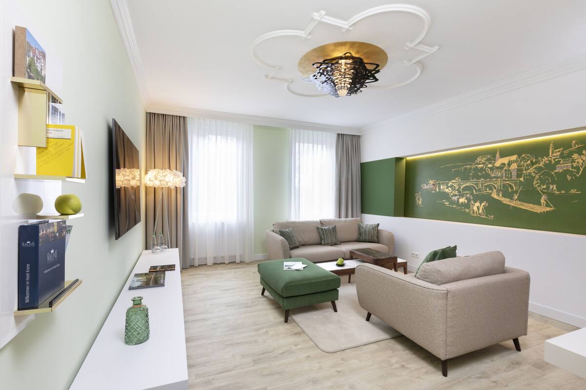 A modern living room with a sofa, ottoman, and coffee table. There is a wall-mounted TV and a decorative light fixture.