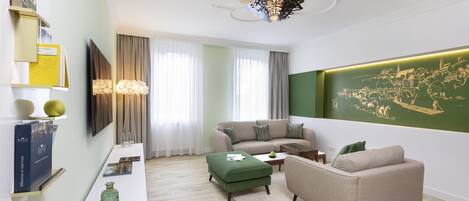 A modern living room with a sofa, ottoman, and coffee table. There is a wall-mounted TV and a decorative light fixture.