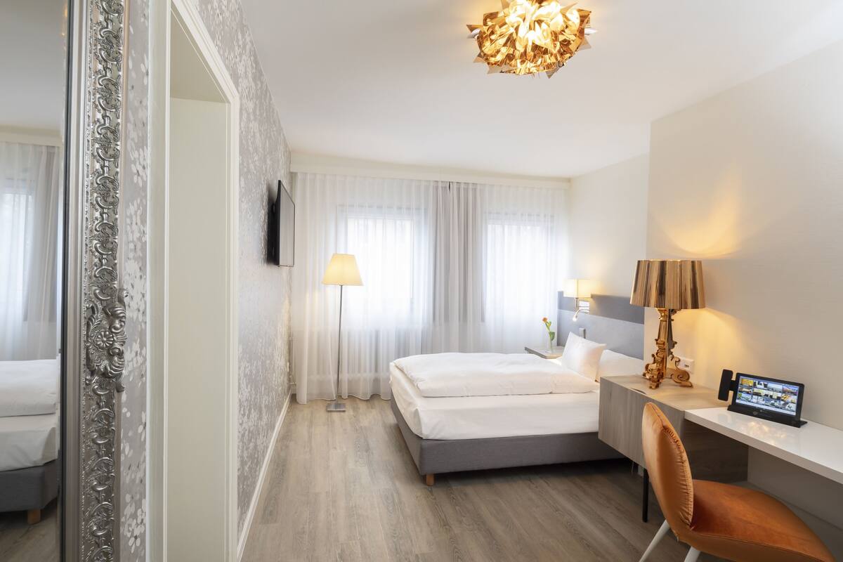 A modern hotel room with a bed, desk, chair, and a television.
