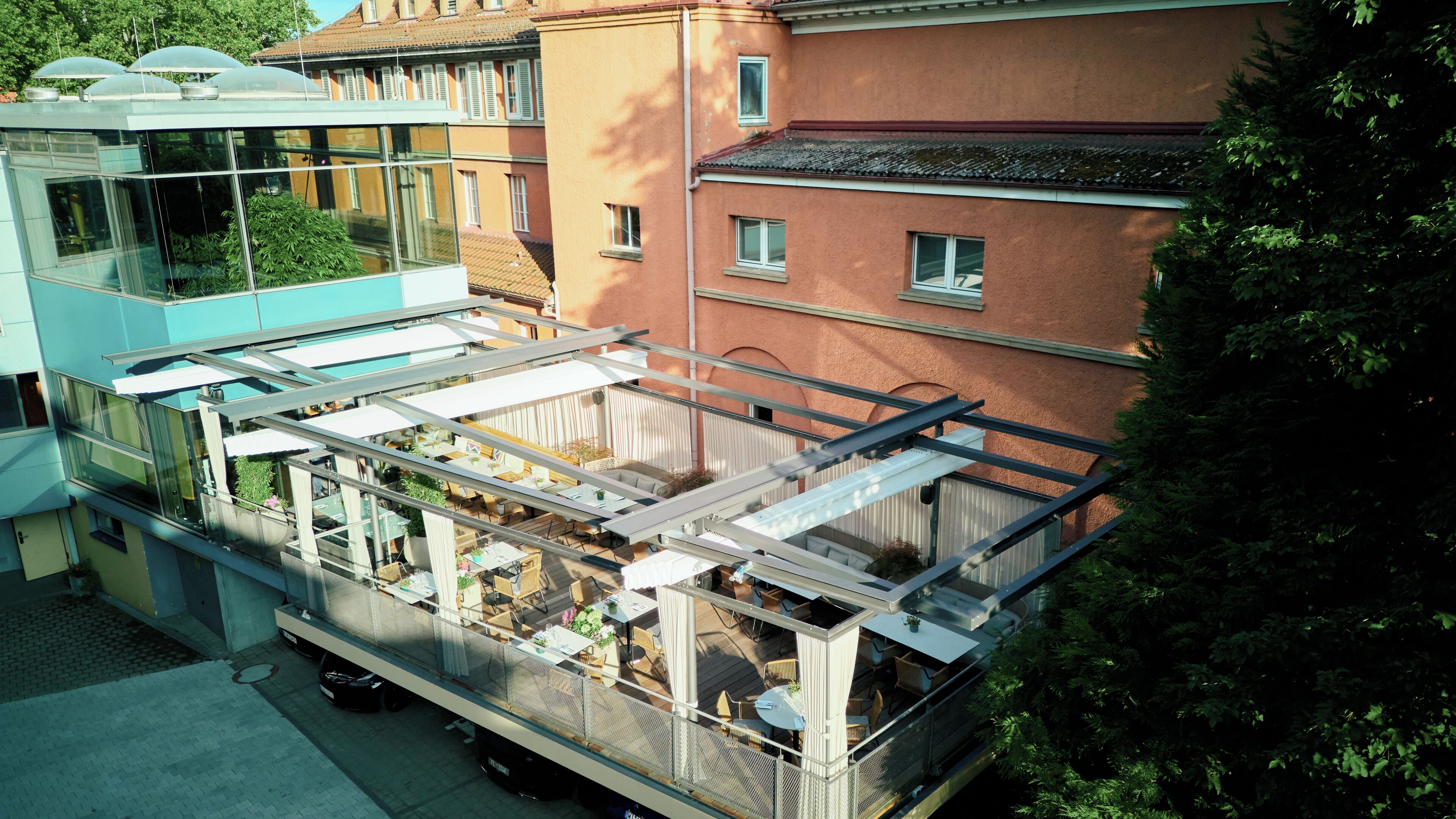 Un bâtiment moderne doté d’une façade en verre, d’un espace extérieur aménagé pour s’asseoir et offrant une vue sur les immeubles voisins.
