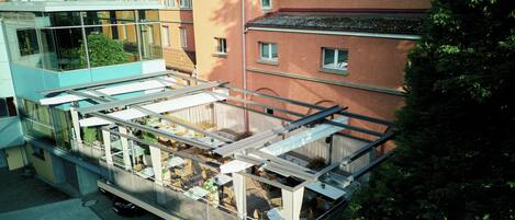 Un bâtiment moderne doté d’une façade en verre, d’un espace extérieur aménagé pour s’asseoir et offrant une vue sur les immeubles voisins.