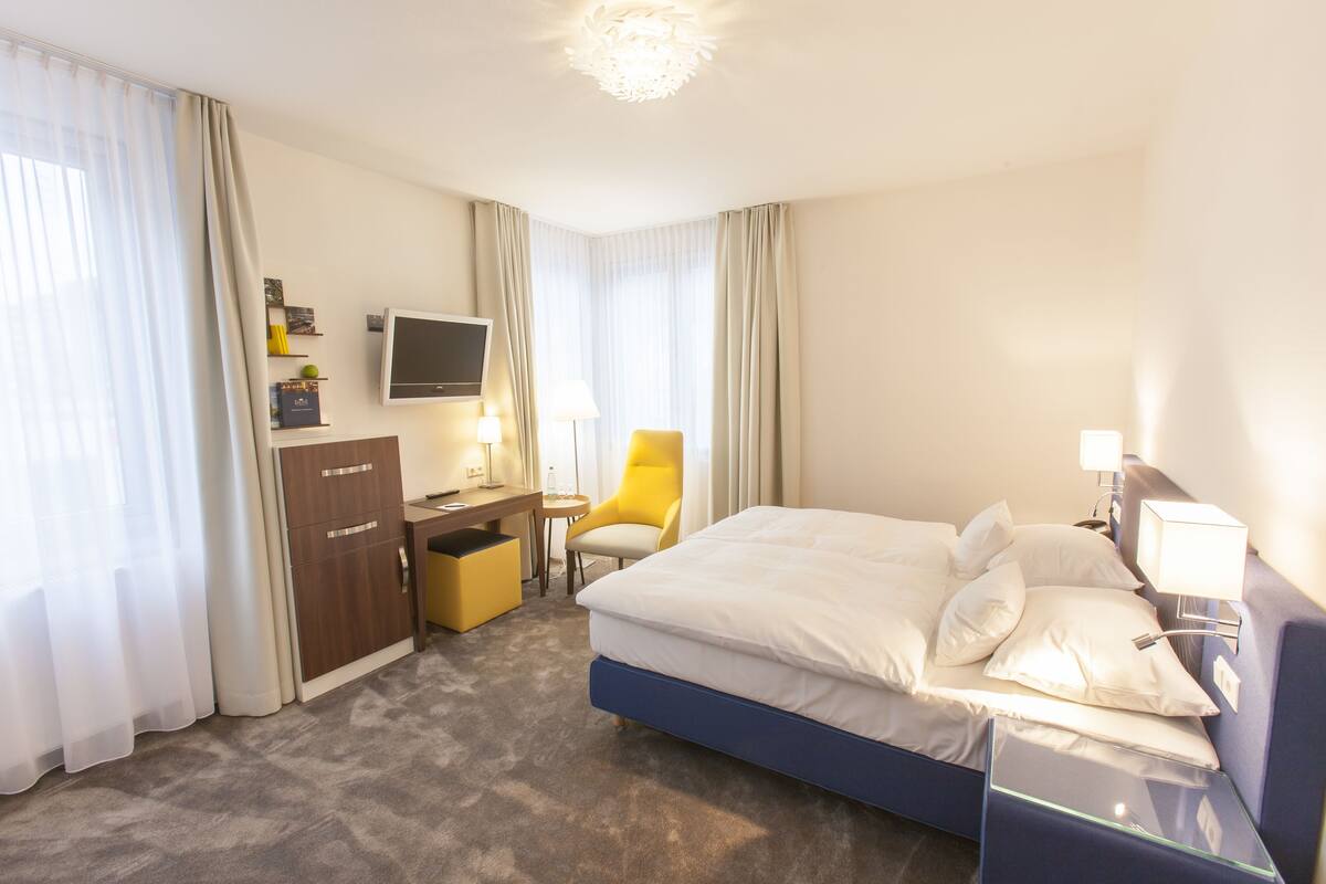 A hotel room with a bed, a desk, a chair, a TV, and a wardrobe.