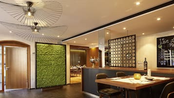 A modern dining area with a wooden table, chairs, a green vertical garden wall, and a ceiling with a geometric light fixture.