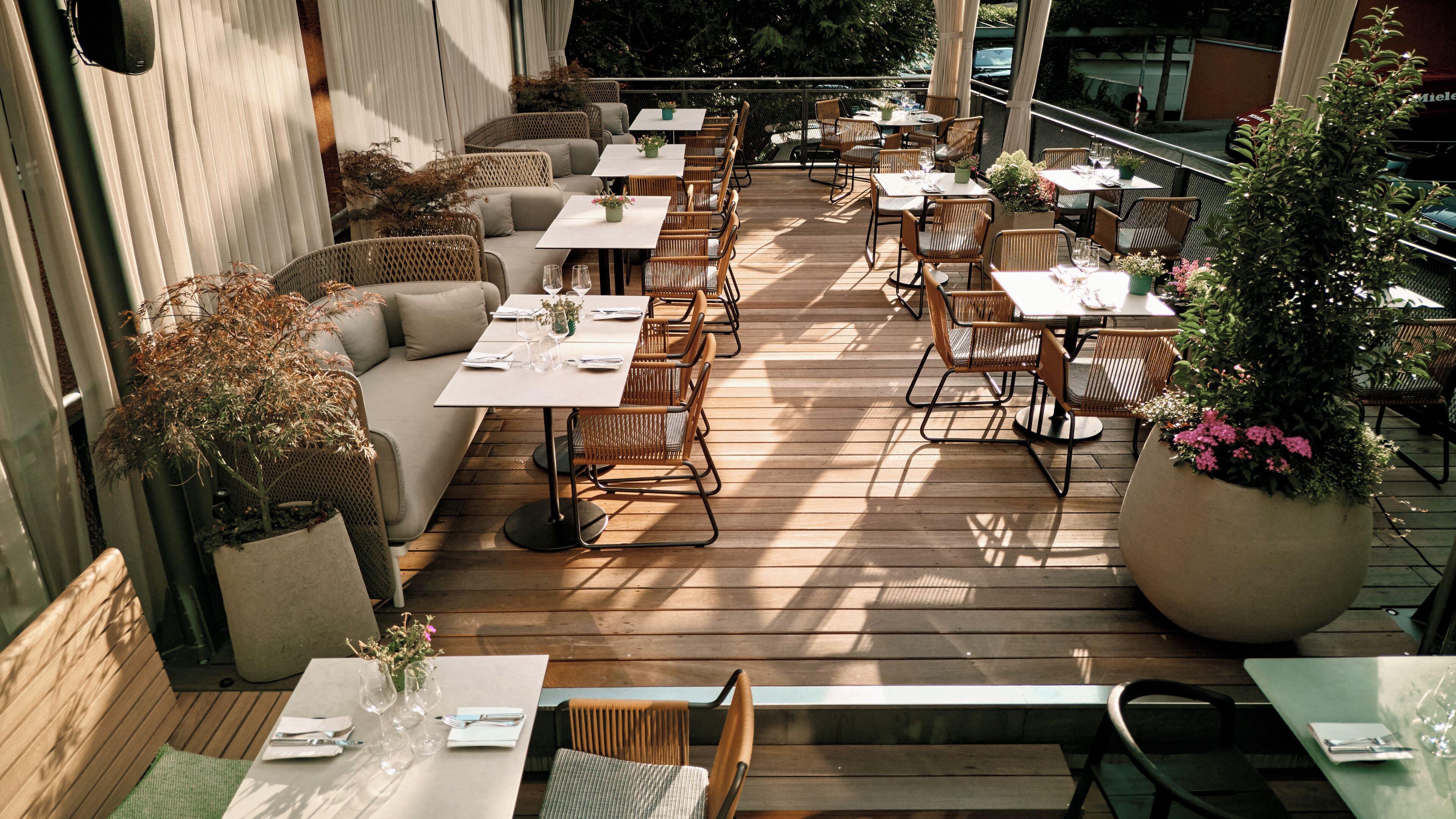 Un espacio de comedor al aire libre con varias mesas y sillas, algunas con cojines.