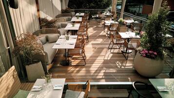 Un espacio de comedor al aire libre con varias mesas y sillas, algunas con cojines.