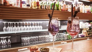 Dos vasos de martini con zarzamoras sobre una barra, con una variedad de botellas al fondo.