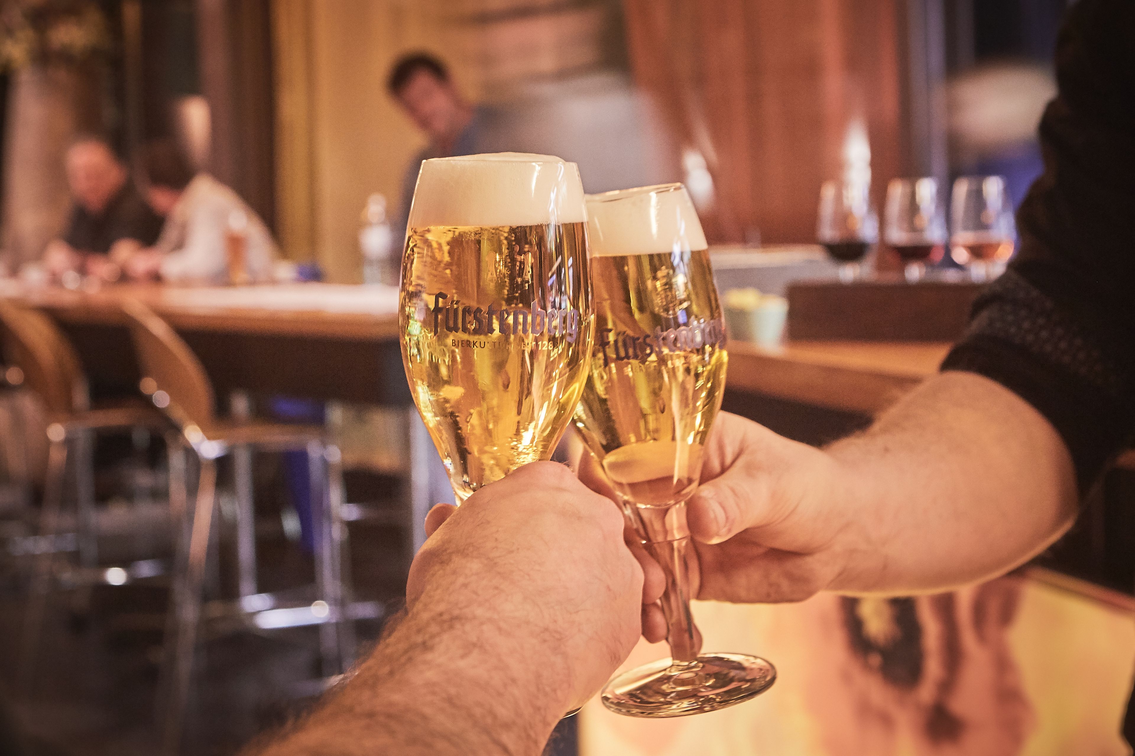 Zwei Personen stoßen in einer Bar mit Biergläsern an.