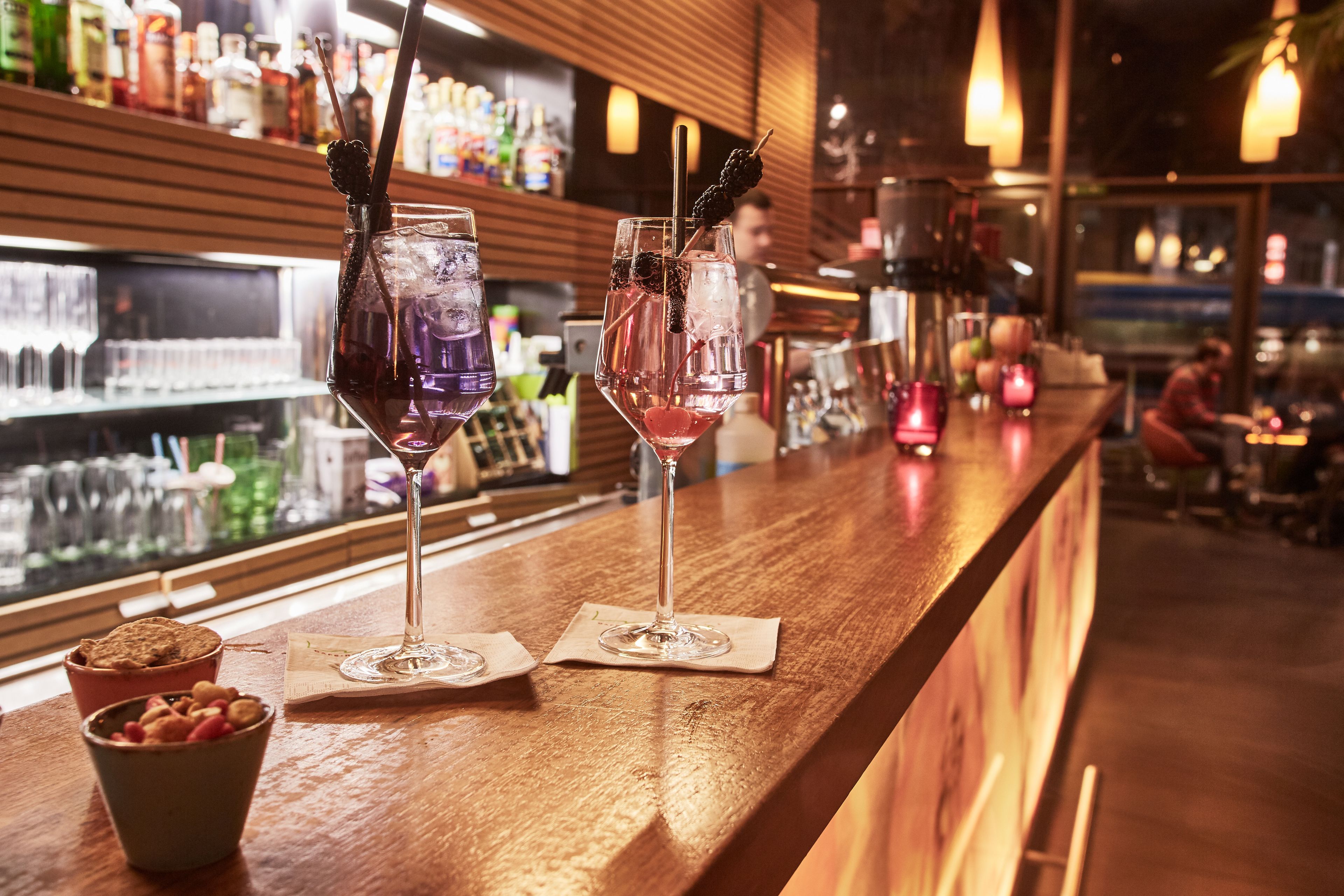 Eine Bar mit zwei Cocktailgläsern, einer Spirituosenflasche und einer Schale Snacks.