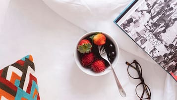 A bowl of fruit with strawberries and rambutan on a white surface, a pair of glasses, and a book with a black and white cover.