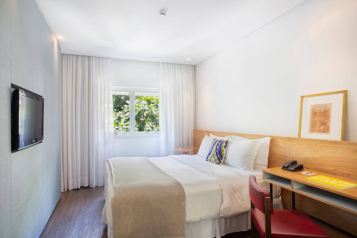 Una habitación de hotel con cama, escritorio, teléfono y televisor.