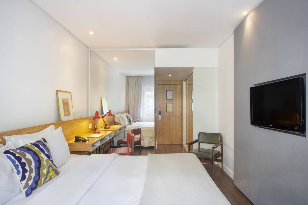 Habitación de hotel con cama, escritorio, silla, televisor y puerta que da a otra habitación.