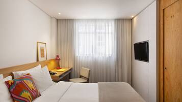Una habitación de hotel con cama, escritorio, silla, televisión y ventana con cortinas.