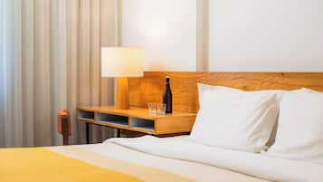 Una habitación de hotel con una cama, una mesita de noche de madera, una lámpara, una botella y dos vasos.