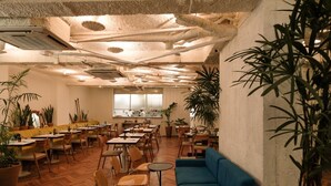 A spacious indoor area with multiple tables and chairs, a blue sofa, and several potted plants. - Ipanema Inn (Rio de Janeiro)