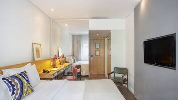 Une chambre d’hôtel avec un grand lit, un bureau avec une chaise, un téléviseur fixé au mur et une porte donnant sur une autre pièce.