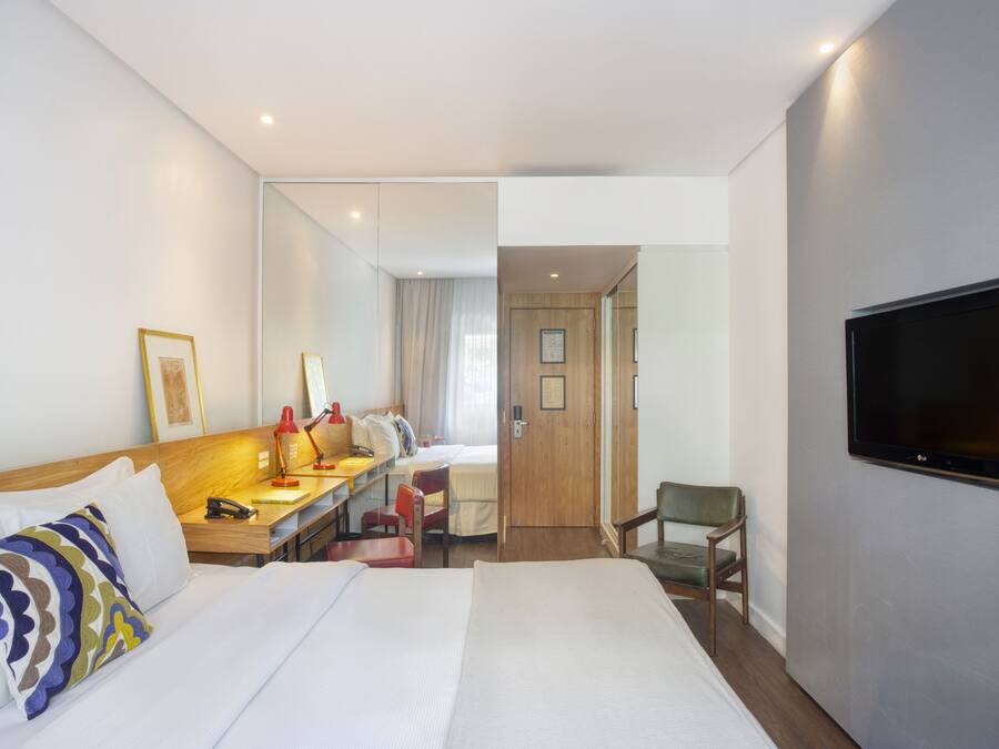 Une chambre d’hôtel avec un grand lit, un bureau avec une chaise, un téléviseur fixé au mur et une porte donnant sur une autre pièce.
