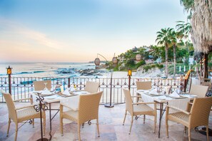 A seaside restaurant with wicker furniture and tables set for dining, overlooking the ocean. - Cabo Surf Hotel & Spa (San José del Cabo)