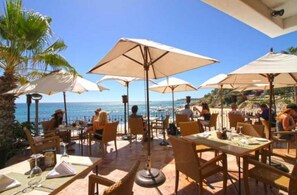 Un espace extérieur aménagé pour les repas, avec des tables, des chaises, des parasols et une vue sur la mer.