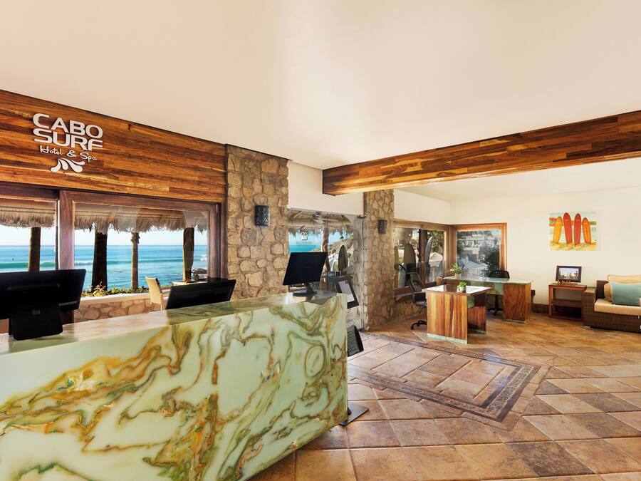 A hotel lobby with a reception desk, computers, a stone wall, and a view of the ocean.