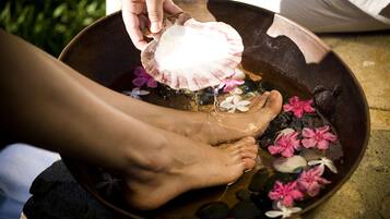 A person washing feet in a bowl with flowers and a shell.