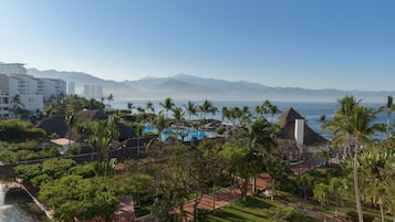 A resort with a pool, palm trees, and a view of the ocean and mountains.