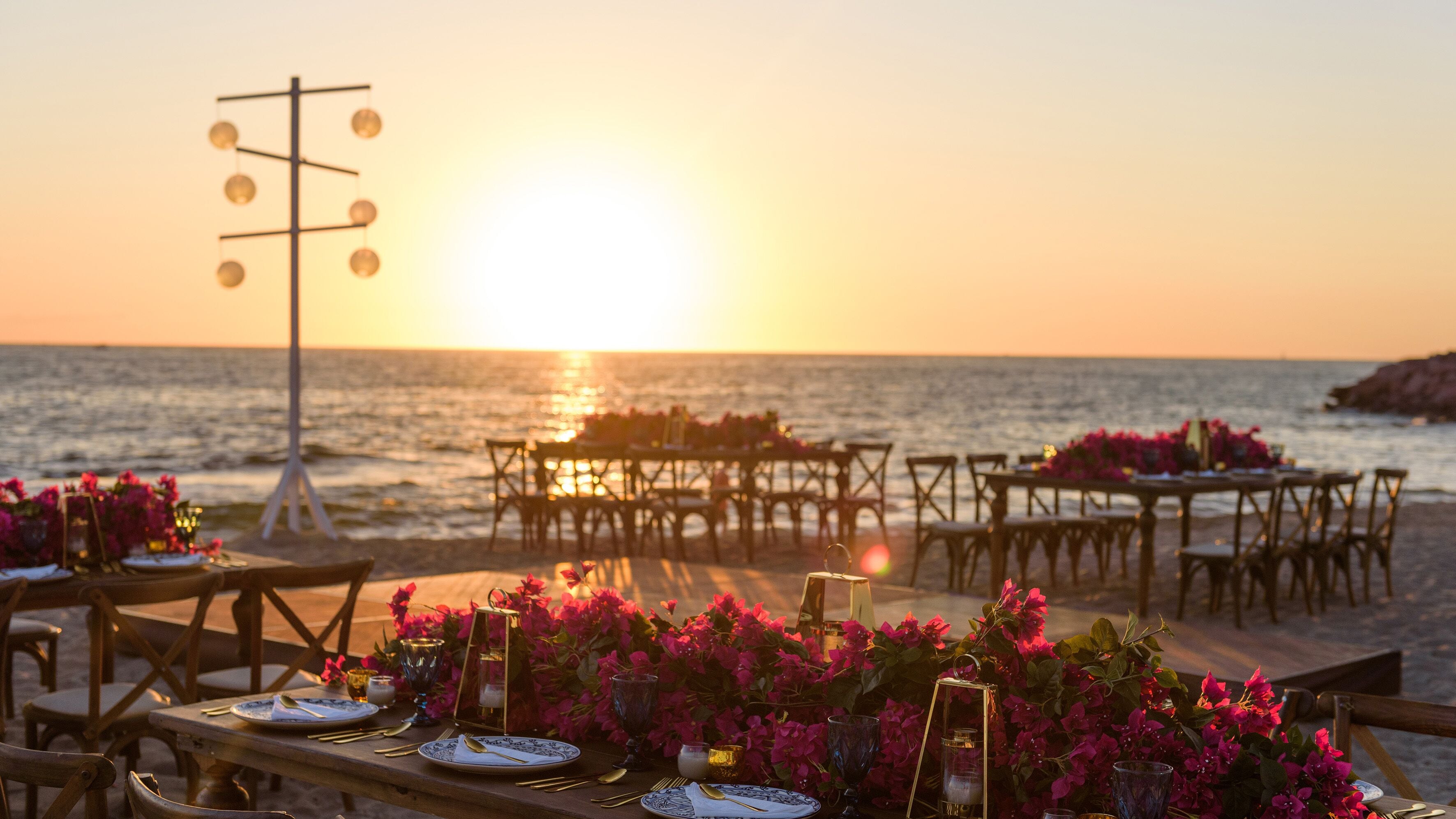 A beachside dining setup with tables and chairs arranged for an outdoor meal, overlooking the sea.
