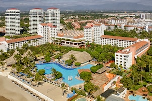 Un resort con una piscina central, varios edificios altos y abundante vegetación.