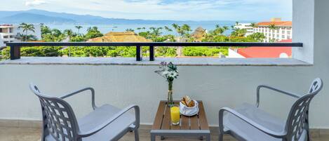 A balcony with two chairs, a small table with a vase of flowers, a glass of orange juice, and a basket of bread.