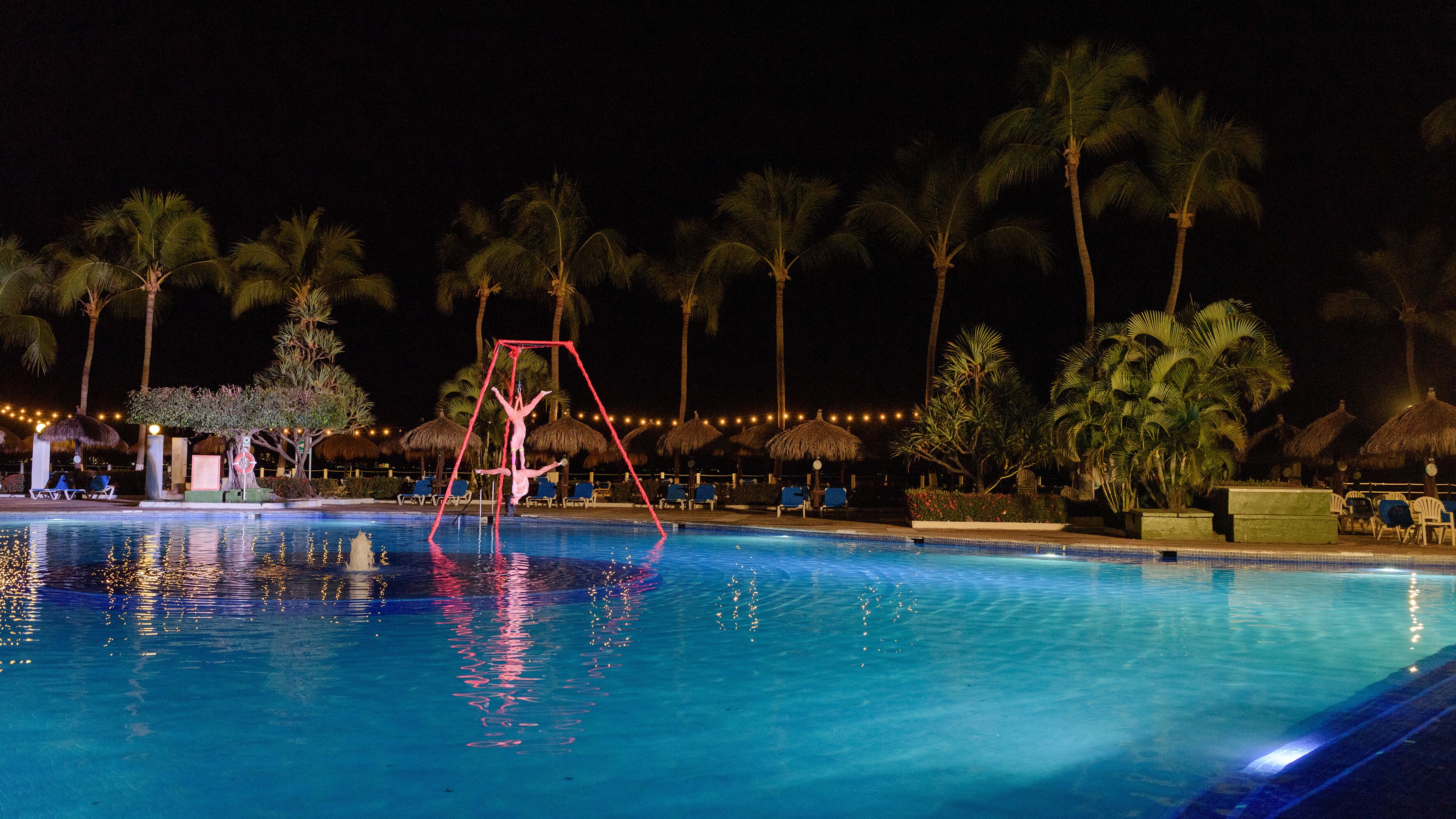 A nighttime pool area with a swing set, palm trees, and lounge chairs.