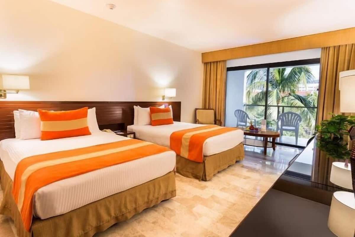 A hotel room with two beds, a small table, a chair, and a view of palm trees.