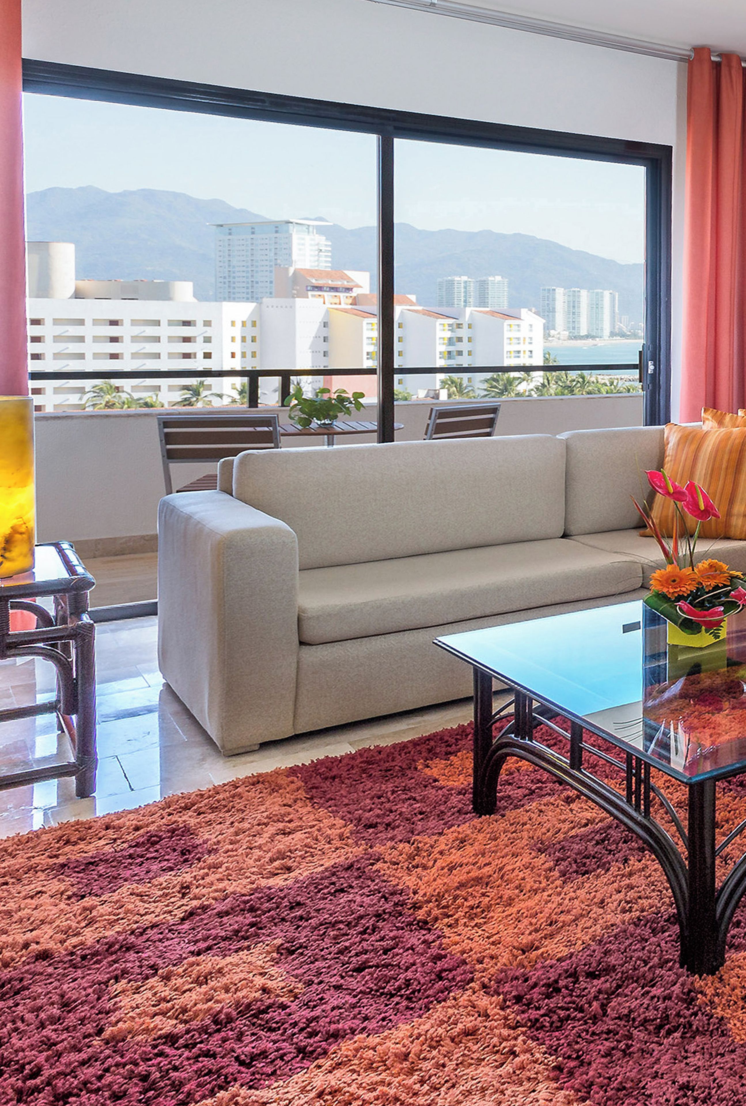 A modern living room with a sofa, a coffee table, and a view of a cityscape through large windows.
