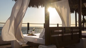A beachside bed with a canopy, a bottle of champagne, and a glass on the table.
