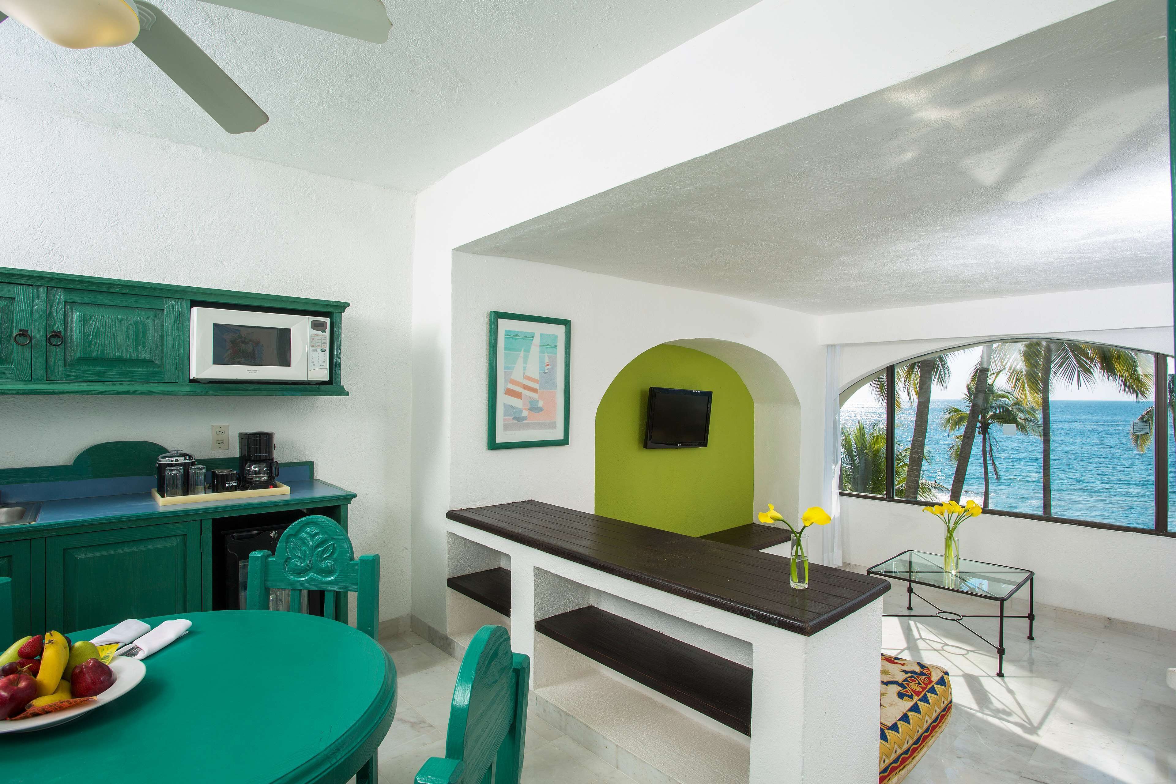 A kitchen with a microwave, a dining table with chairs, a small table with a vase, and a view of the ocean through a window.