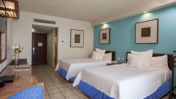 Una habitación de hotel con dos camas, un escritorio con silla, un florero con flores y cuadros en la pared.