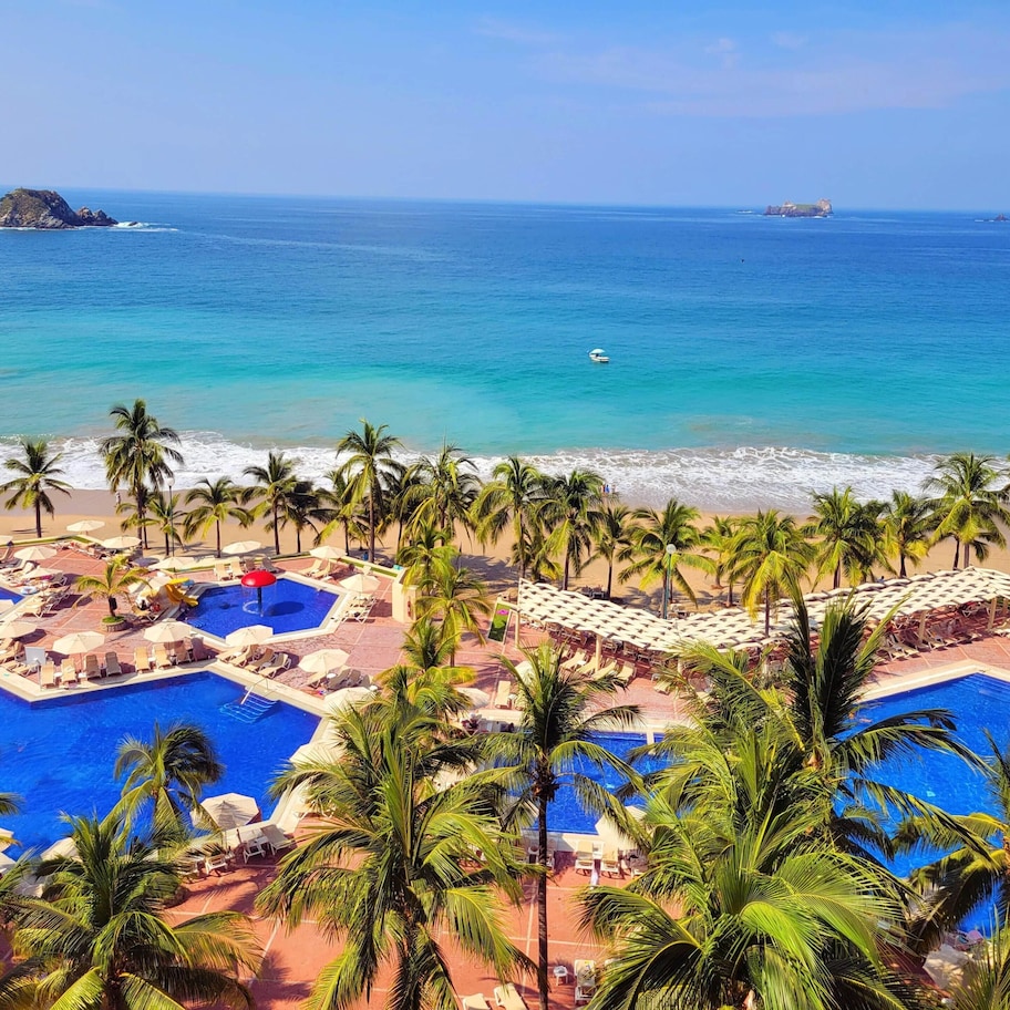 A resort with a swimming pool, beach, and palm trees.