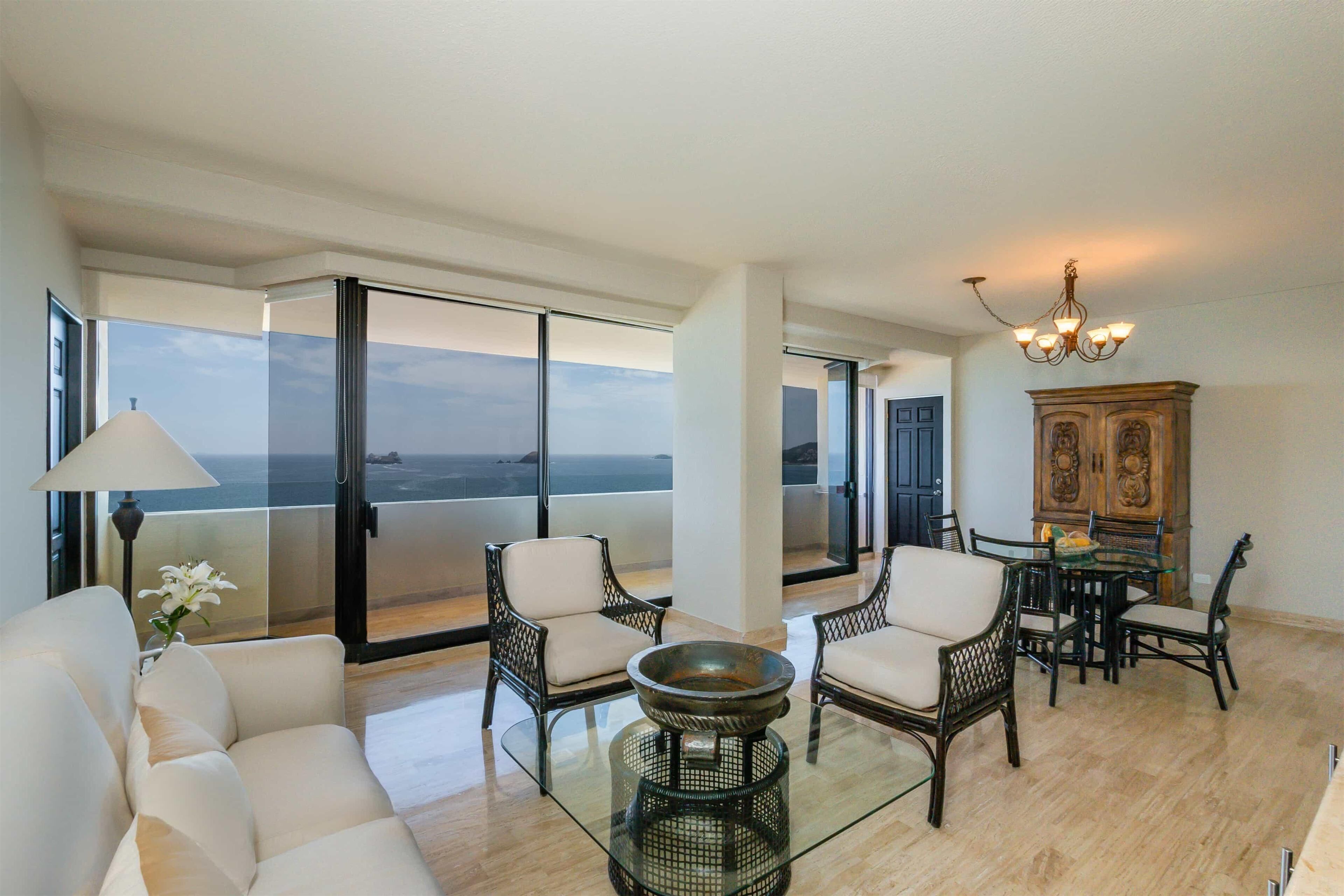 A spacious living area with a glass table, chairs, a sofa, and a view of the ocean.