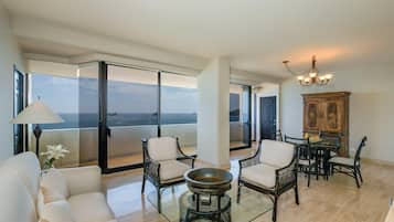 A spacious living area with a glass table, chairs, a sofa, and a view of the ocean.